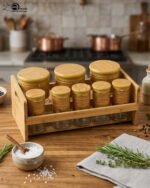 A high-angle view of a glass spice jar and salt shaker set held within a natural bamboo wooden stand, displayed on a rustic wooden table with fresh herbs.