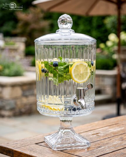 Elegant 4.5 Liter ribbed glass beverage dispenser with a silver spigot and decorative stand, filled with water, lemon slices, blueberries, and mint leaves on an outdoor wooden table, as shown in 2.jpg.