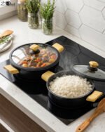 Two black, Made-in-Turkey granite non-stick casserole pots (26cm and 30cm) with wooden-look handles and rubber-rimmed lids sitting on a marble kitchen countertop.