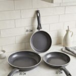 Three sizes of grey diamond-infused non-stick frying pans (20cm, 22cm, 26cm) arranged on a kitchen counter.