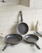 Three sizes of grey diamond-infused non-stick frying pans (20cm, 22cm, 26cm) arranged on a kitchen counter.