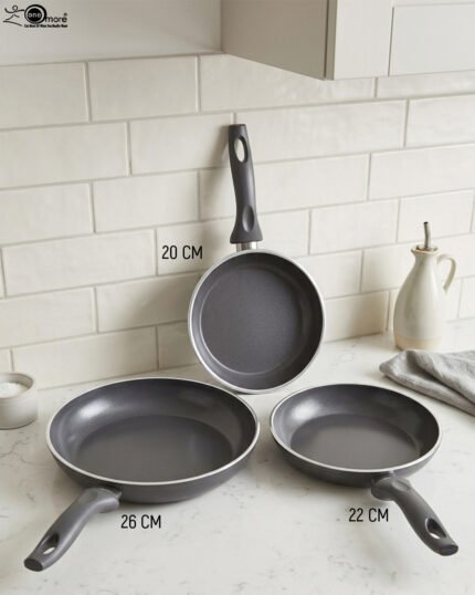 Three sizes of grey diamond-infused non-stick frying pans (20cm, 22cm, 26cm) arranged on a kitchen counter.