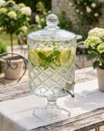 Elegant 4.5-liter diamond-cut glass beverage dispenser filled with infused lemon and cucumber water on an outdoor garden party table, featured in 2.jpg.