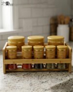 A high-angle view of a glass spice jar and salt shaker set held within a natural bamboo wooden stand, displayed on a rustic wooden table with fresh herbs.