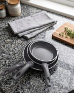 Three sizes of grey diamond-infused non-stick frying pans (20cm, 22cm, 26cm) arranged on a kitchen counter.