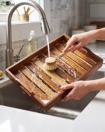 Two stacked, high-quality wooden serving trays resting on a kitchen countertop with a copper kettle and plant in the background.