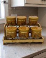 A set of six glass spice jars with wooden-look lids arranged on a matching tiered wooden stand, sitting on a kitchen countertop.
