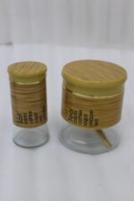 A high-angle view of a glass spice jar and salt shaker set held within a natural bamboo wooden stand, displayed on a rustic wooden table with fresh herbs.