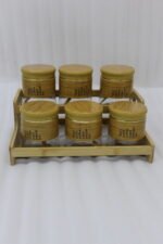 A set of six glass spice jars with wooden-look lids arranged on a matching tiered wooden stand, sitting on a kitchen countertop.