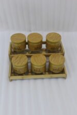 A set of six glass spice jars with wooden-look lids arranged on a matching tiered wooden stand, sitting on a kitchen countertop.