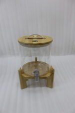 Three glass beverage dispensers of varying heights, each featuring a bamboo lid and resting on a wooden stand, displayed on a table next to a buffet burner.