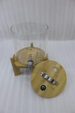 Three glass beverage dispensers of varying heights, each featuring a bamboo lid and resting on a wooden stand, displayed on a table next to a buffet burner.