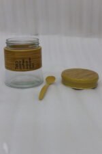 A high-angle view of a glass spice jar and salt shaker set held within a natural bamboo wooden stand, displayed on a rustic wooden table with fresh herbs.