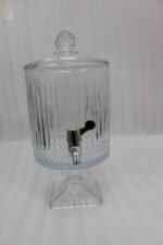 Elegant 4.5 Liter ribbed glass beverage dispenser with a silver spigot and decorative stand, filled with water, lemon slices, blueberries, and mint leaves on an outdoor wooden table, as shown in 2.jpg.