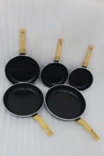 A collection of Turkish-made diamond-infused non-stick frying pans in various sizes ranging from 20cm to 30cm, displayed on a kitchen wall and countertop at OneMore.