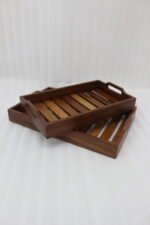 Two stacked, high-quality wooden serving trays resting on a kitchen countertop with a copper kettle and plant in the background.