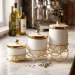 A set of three white ceramic jars with gold lids and spherical handles, elegantly arranged in a decorative gold metal cart stand against a white background.