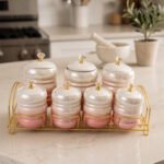 Luxury pink and white ceramic storage jar set with crystal knobs arranged on a modern gold wire rack on a kitchen countertop.