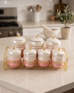 Luxury pink and white ceramic storage jar set with crystal knobs arranged on a modern gold wire rack on a kitchen countertop.