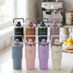 An assortment of colorful 900ml stainless steel tumblers with handles and transparent straw lids arranged neatly on a kitchen counter.