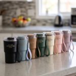 Line-up of colorful 360ml stainless steel travel tumblers with matching carrying straps and clear lids displayed on a kitchen counter.