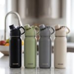 Four Dodge 630mL stainless steel water bottles in black, sage green, grey, and beige lined up on a kitchen counter.