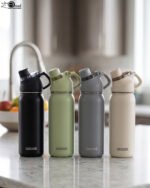 Four Dodge 630mL stainless steel water bottles in black, sage green, grey, and beige lined up on a kitchen counter.