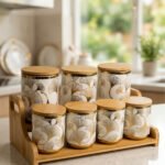 Luxury white and gold ceramic kitchen storage jar set with wooden lids arranged on a wooden display stand in a modern kitchen.