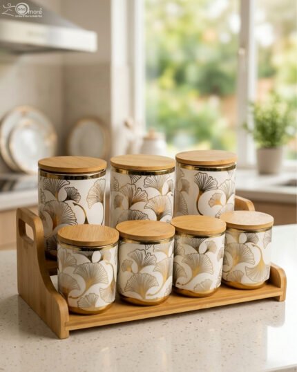Luxury white and gold ceramic kitchen storage jar set with wooden lids arranged on a wooden display stand in a modern kitchen.