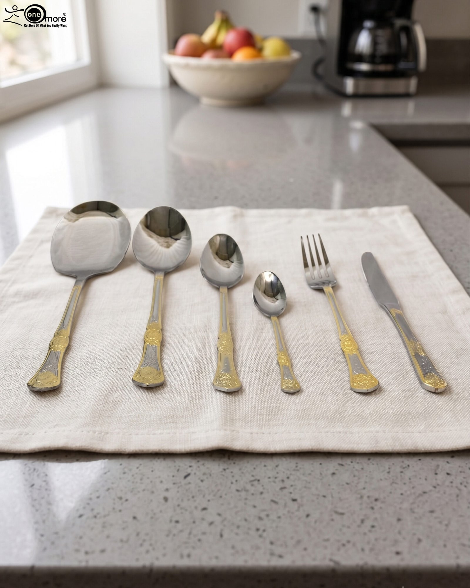 1 Six-piece gold accented stainless steel flatware set displayed on a linen mat including rice spoons, fork, knife, and serving spoons.