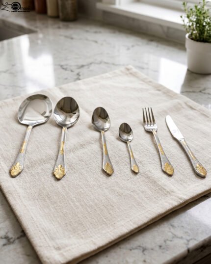 Six-piece luxury stainless steel cutlery set featuring textured handles with gold filigree details displayed on a beige linen napkin.