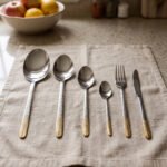 Stainless steel cutlery set with textured gold handles and floral engravings displayed on a beige cloth.