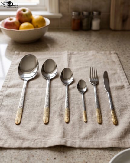 Stainless steel cutlery set with textured gold handles and floral engravings displayed on a beige cloth.