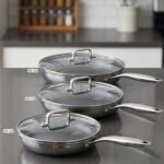 A 3-piece stainless steel cookware set with glass lids featuring 24CM, 26CM, and 28CM sizes displayed neatly on a kitchen counter.