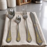 24 piece mirror polish stainless steel cutlery set with ornate gold heart handle detailing on a folded napkin