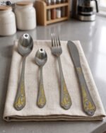 24 piece mirror polish stainless steel cutlery set with ornate gold heart handle detailing on a folded napkin