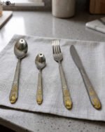 24-piece stainless steel cutlery set featuring gold "Love" engravings on handles, including rice spoon, sweet spoon, fork, and knife on a gray napkin.