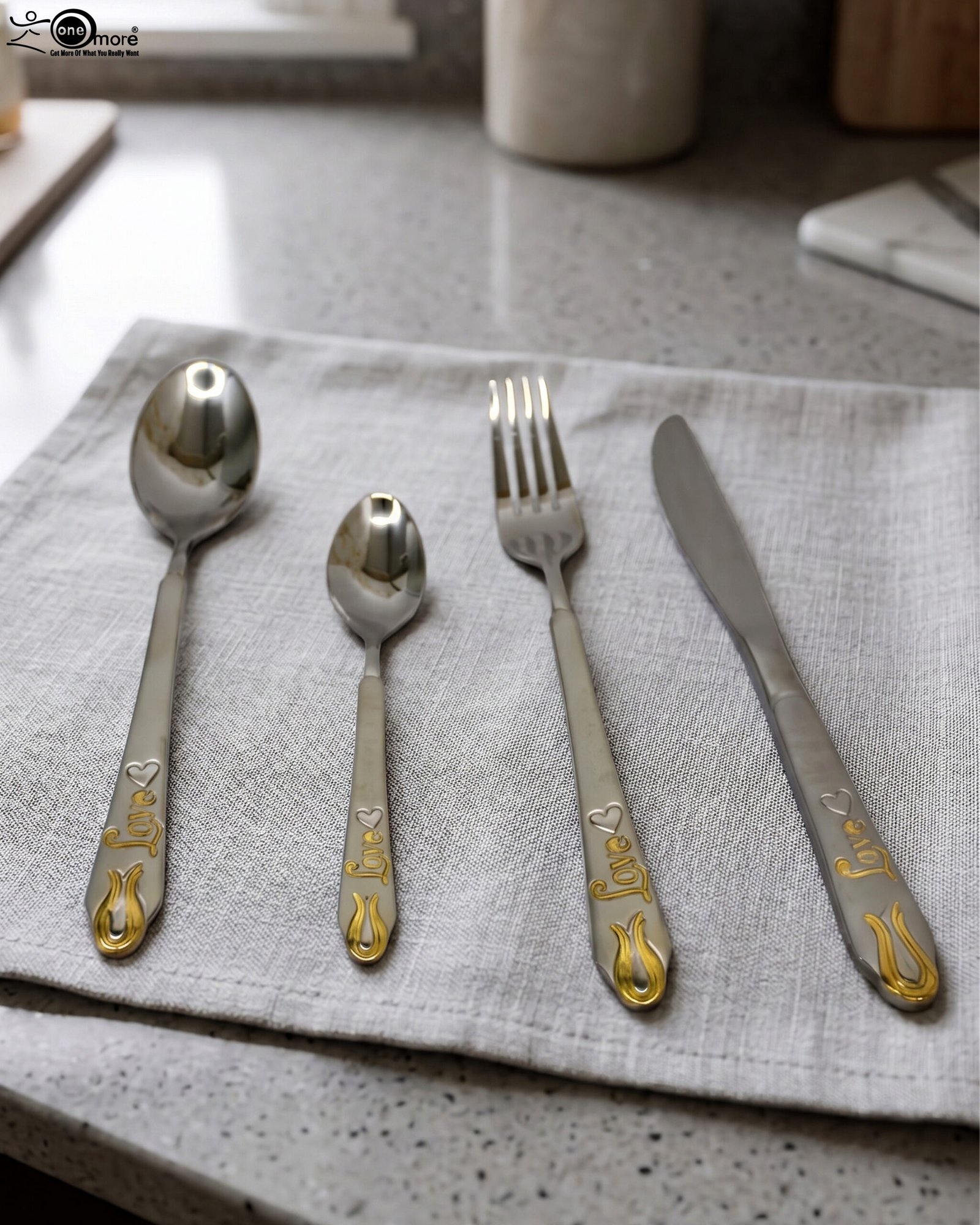 1 24-piece stainless steel cutlery set featuring gold "Love" engravings on handles, including rice spoon, sweet spoon, fork, and knife on a gray napkin.