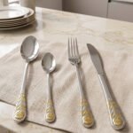 24 piece stainless steel cutlery set with gold rose embossed handles displayed on a cloth napkin