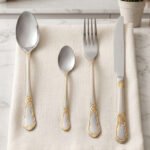 24-piece stainless steel cutlery set with ornate gold embossed handles laid out on a beige linen napkin