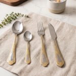 Luxury 24-piece stainless steel cutlery set with ornate gold embossed handles arranged on a linen napkin
