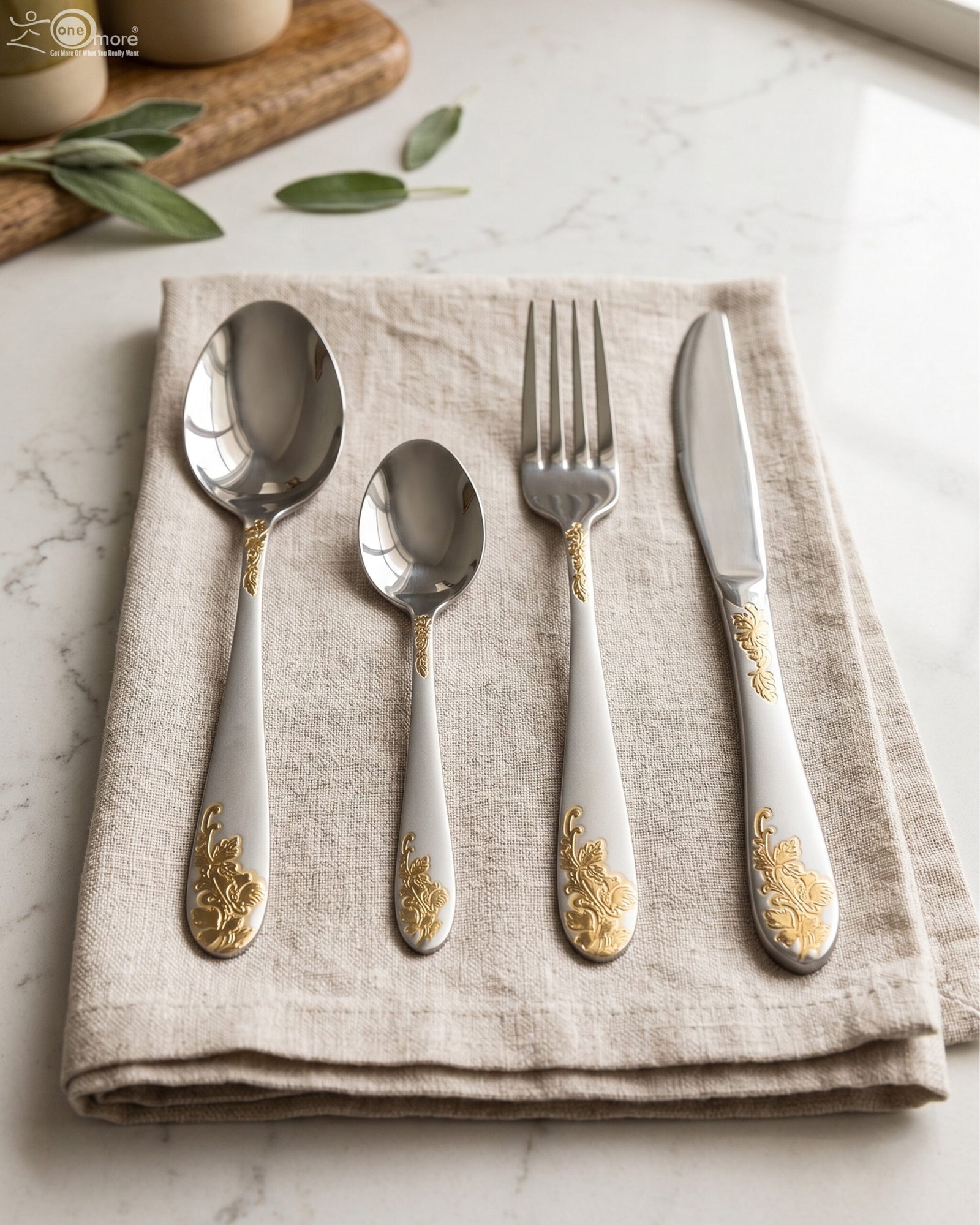 1 24-piece silver stainless steel cutlery set with gold floral embossed handles displayed on a linen napkin.