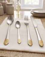 24-piece stainless steel flatware cutlery set with decorative gold handles laid out on a linen cloth
