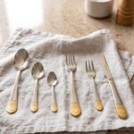 36-piece polished stainless steel cutlery set with ornate gold-accented handles arranged on a linen napkin.