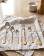 36-piece polished stainless steel cutlery set with ornate gold-accented handles arranged on a linen napkin.
