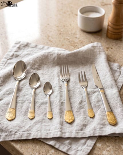 36-piece polished stainless steel cutlery set with ornate gold-accented handles arranged on a linen napkin.