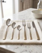 36-piece stainless steel cutlery set with two-tone gold and silver textured handles displayed on a beige napkin.