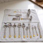 72 piece stainless steel cutlery set with gold detailed handles displayed on a linen mat