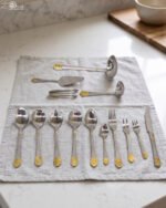 72 piece stainless steel cutlery set with gold detailed handles displayed on a linen mat