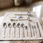 72-piece stainless steel cutlery set with gold-embossed handles arranged on a neutral linen cloth